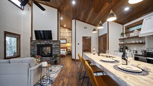 Eine moderne Küche mit Kamin aus Stein, Holzboden und einer Essecke mit Barhocker.