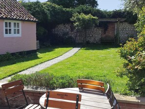 Un giardino con un vialetto lastricato, una panchina in legno e un edificio rosa con una finestra.