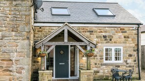 A stone building with a dark entrance door, two windows, and a small outdoor seating area. - South Carolina Farm House (Matlock)