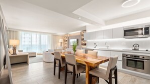 Une cuisine moderne dotée d’appareils électroménagers intégrés, un coin repas avec une table et des chaises en bois, et un salon avec un canapé et une lampe.