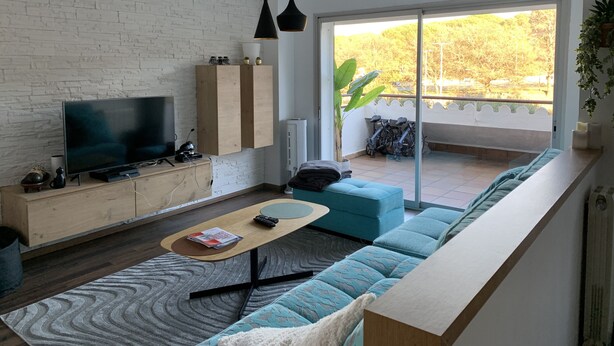A modern living room with a TV, wooden cabinets, a sofa, and a balcony with a view of trees. - Apartment in guarded residence overlooking swimming pool (Platja d'Aro)