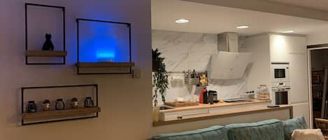 Una sala de estar moderna con un sofá, una mesa de centro y una cocina visible a través de un umbral abierto.
