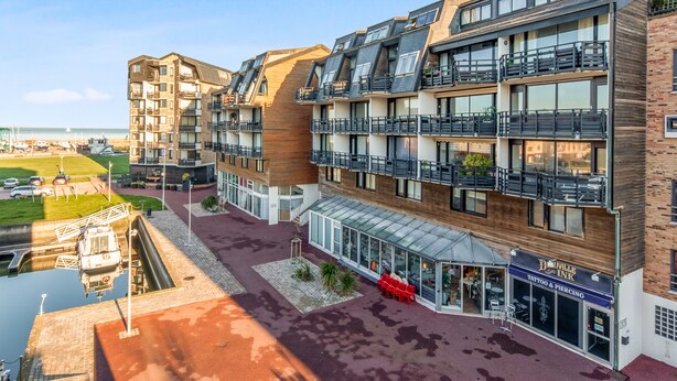 Un edificio moderno de varios pisos con balcones, escaparate de vidrio y vista despejada a la playa.