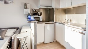 Una cocina compacta con microondas, cafetera y un lavamanos pequeño.
