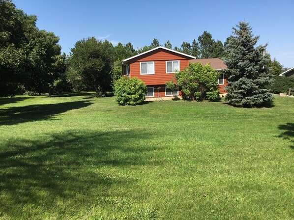 Une maison rouge avec une pelouse bien entretenue et plusieurs arbres dans le jardin.