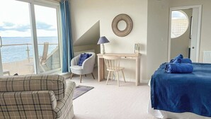Un dormitorio con cama, escritorio, silla, sofá y vistas al mar.