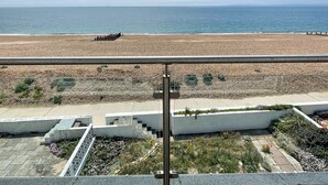 Vista de una playa desde un balcón con barandilla, cielo despejado y el océano al fondo.