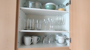 A kitchen cabinet with shelves holding glassware, mugs, and a coffee maker. - Cozy apartmen in center Sablon (Bruxelles)
