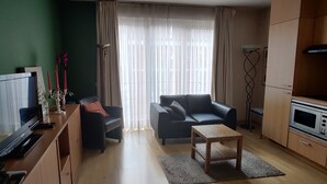 A living room with a TV, sofa, coffee table, and kitchen area with a microwave. - Cozy apartmen in center Sablon (Bruxelles)