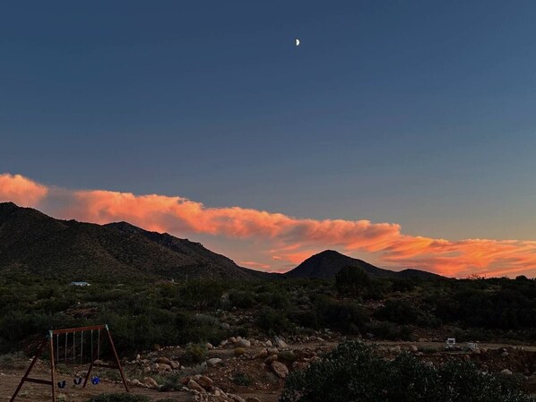 A desert landscape with mountains, a swing set, and a small structure in the foreground.