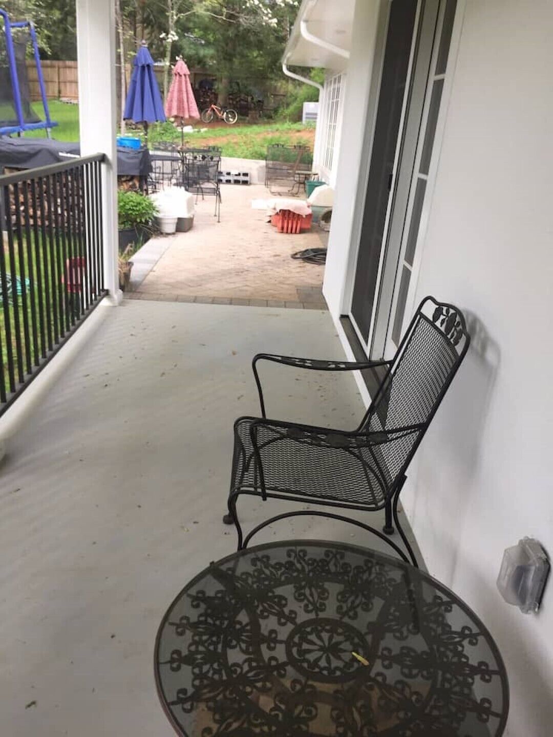 Un porche cubierto con una silla y una mesa de metal, una cerca de madera y mobiliario de exterior.