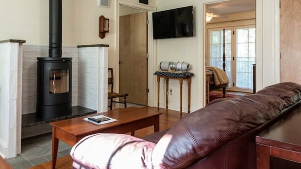 A living room with a black wood stove, a leather sofa, a wooden coffee table, and a television mounted on the wall. - Rugby Road Residential -RRR- near UVa and downtown (Charlottesville)