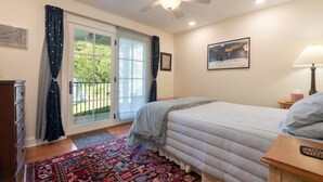 A bedroom with a bed, a nightstand, a lamp, a ceiling fan, a window with curtains, and a door leading to a balcony. - Rugby Road Residential -RRR- near UVa and downtown (Charlottesville)