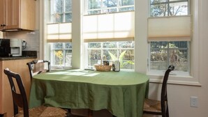 A dining area with a table covered by a green tablecloth, surrounded by wooden chairs. There is a window with blinds, and a kitchen area with a coffee maker and a microwave is visible to the left. - Rugby Road Residential -RRR- near UVa and downtown (Charlottesville)