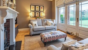 A living room with a fireplace, a sofa, an ottoman, and a large window with a view of greenery. - 1 bedroom accommodation in Willoughby (Willoughby)