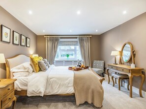 A bedroom with a bed, bedside tables, a dresser, a chair, a window with curtains, and framed pictures on the wall.