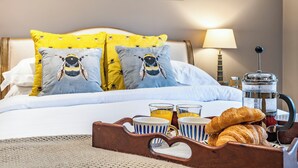 A neatly made bed with bee-themed pillows, a tray with croissants and coffee, and framed floral artwork on the wall. - 1 bedroom accommodation in Willoughby (Willoughby)