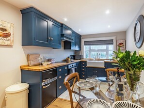 A modern kitchen with dark blue cabinets, a wooden countertop, and a dining area with a glass table set for four.