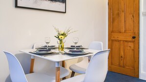 A dining table set with plates, cutlery, and glasses, flanked by white chairs, with a wooden door and a framed picture on the wall. - A delightful haven for walkers and cyclists. (Skipton)