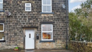 A stone-built house with a white door, two windows, and a satellite dish. - A delightful haven for walkers and cyclists. (Skipton)