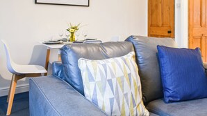 A modern living room with a grey sofa, a dining table set with plates and glasses, and a framed abstract painting on the wall. - A delightful haven for walkers and cyclists. (Skipton)