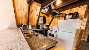 A kitchen with granite countertops, stainless steel sink, white appliances, and wooden walls. - Whispering Waters A-frame (Hocking Hills Area) (Rockbridge)