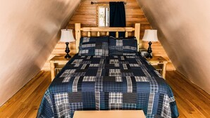 A cozy attic bedroom with a wooden sloped ceiling, a bed with a plaid quilt, two bedside lamps, and a small wooden bench. - Whispering Waters A-frame (Hocking Hills Area) (Rockbridge)