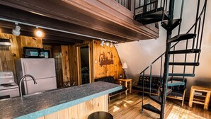 A kitchen with a wooden interior, a black staircase, and a bar area with stools. - Whispering Waters A-frame (Hocking Hills Area) (Rockbridge)