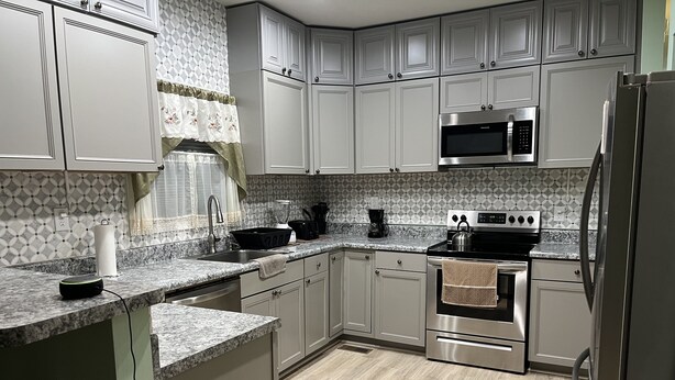A modern kitchen with grey cabinets, a stainless steel refrigerator, a microwave, and an oven. - 1400 Square feet of space, isolate in  three acres lot. (Sutherland)
