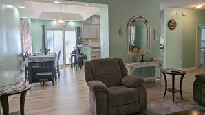 A spacious living room with a ceiling fan, a dining area with a table and chairs, and a kitchen in the background. - 1400 Square feet of space, isolate in  three acres lot. (Sutherland)