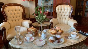 Une salle à manger élégante, avec deux fauteuils rembourrés, une table ronde agrémentée d’un service à thé et une lampe rouge.