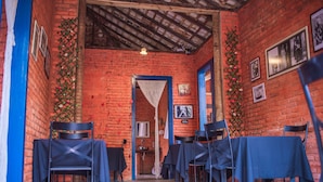 A brick-walled room with a high ceiling, a door leading to another area, and tables with chairs set up for dining. - Pousada Recanto da Lua - Alto Caparaó (Alto Caparao)