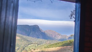 A view through a window of a building with red roofs and brick walls, overlooking a hilly landscape with a mountain in the distance. - Pousada Recanto da Lua - Alto Caparaó (Alto Caparao)