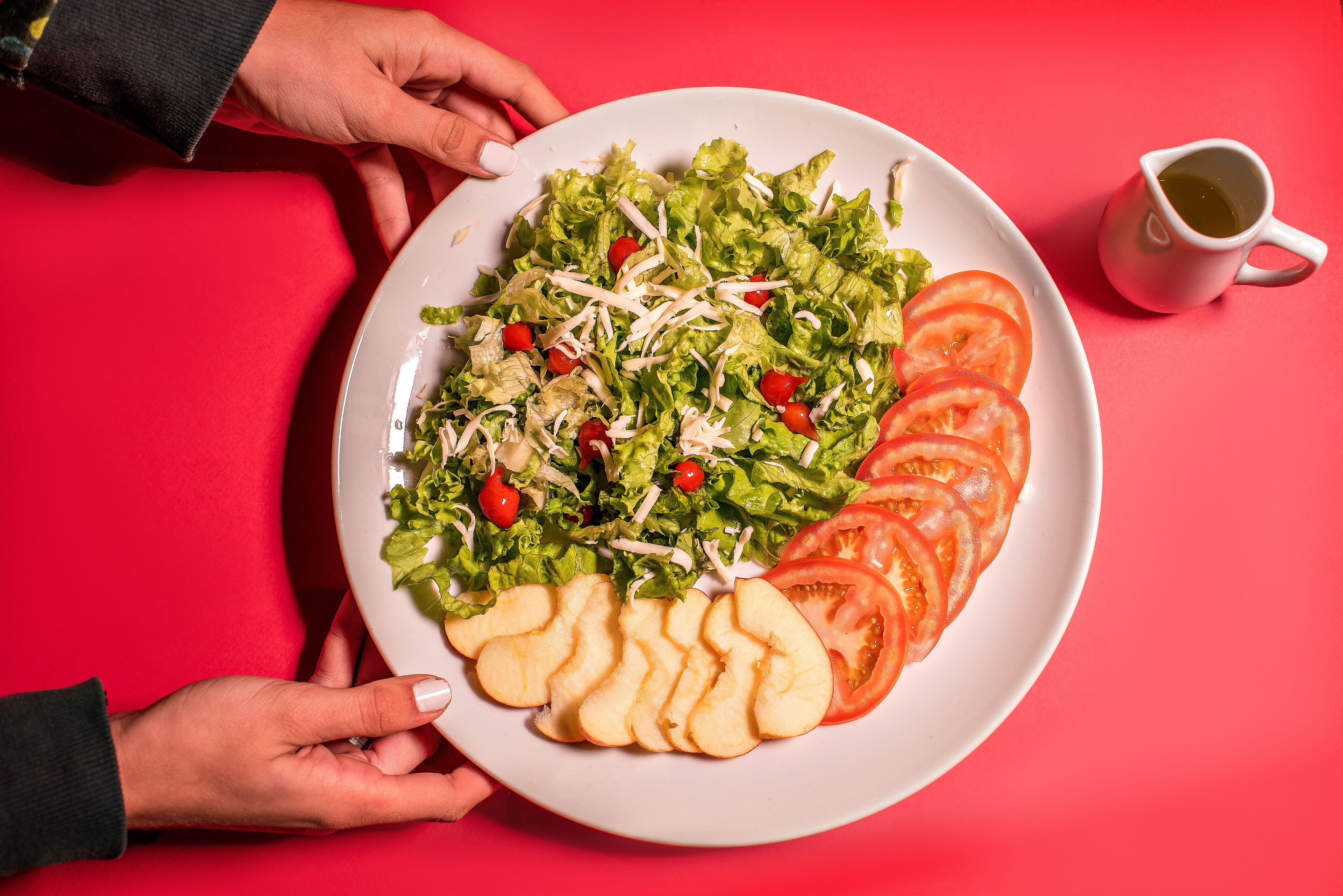 A plate of salad with lettuce, tomatoes, and shredded cheese, held by hands against a red background.