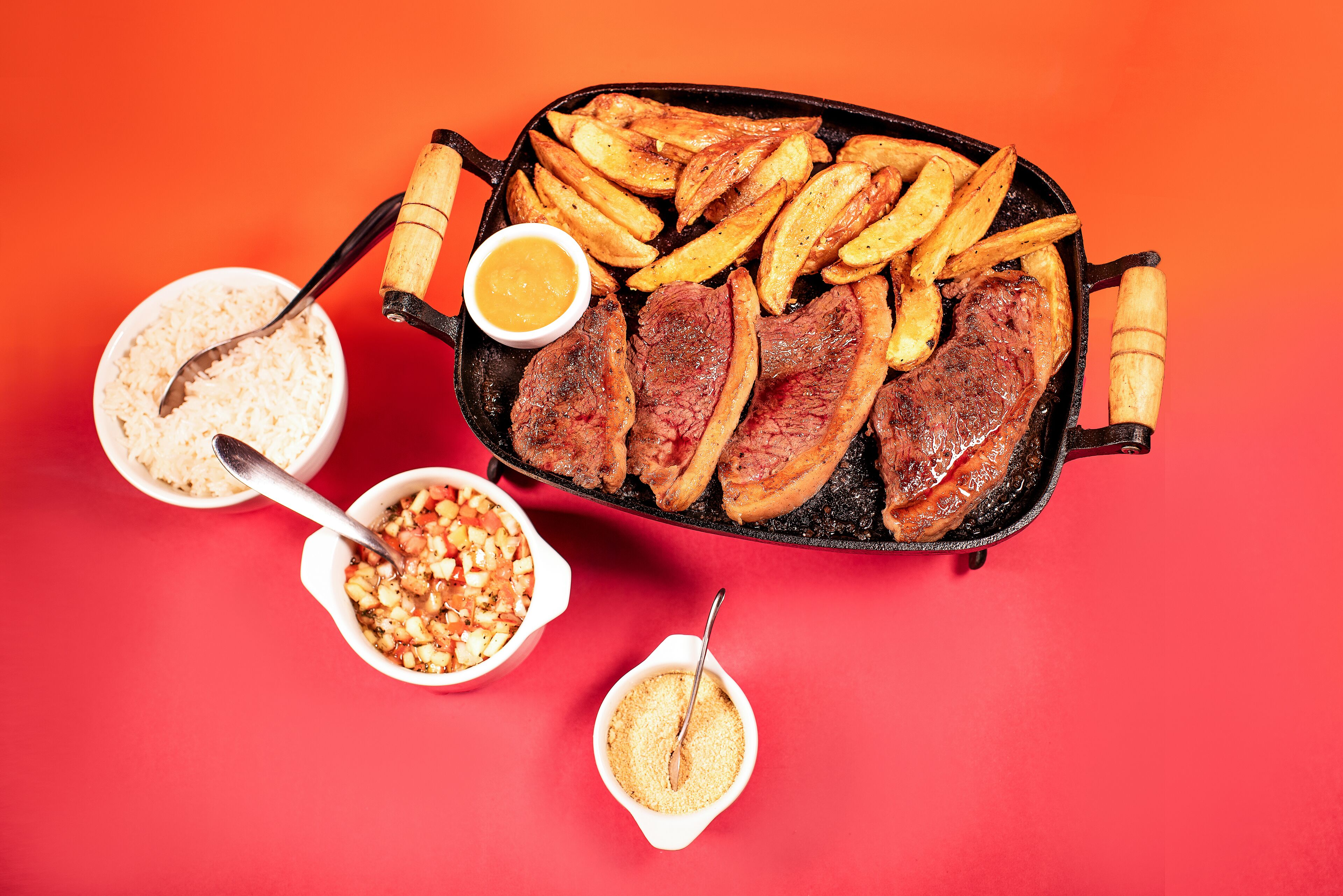 A skillet with steak and fries, accompanied by small bowls of condiments.