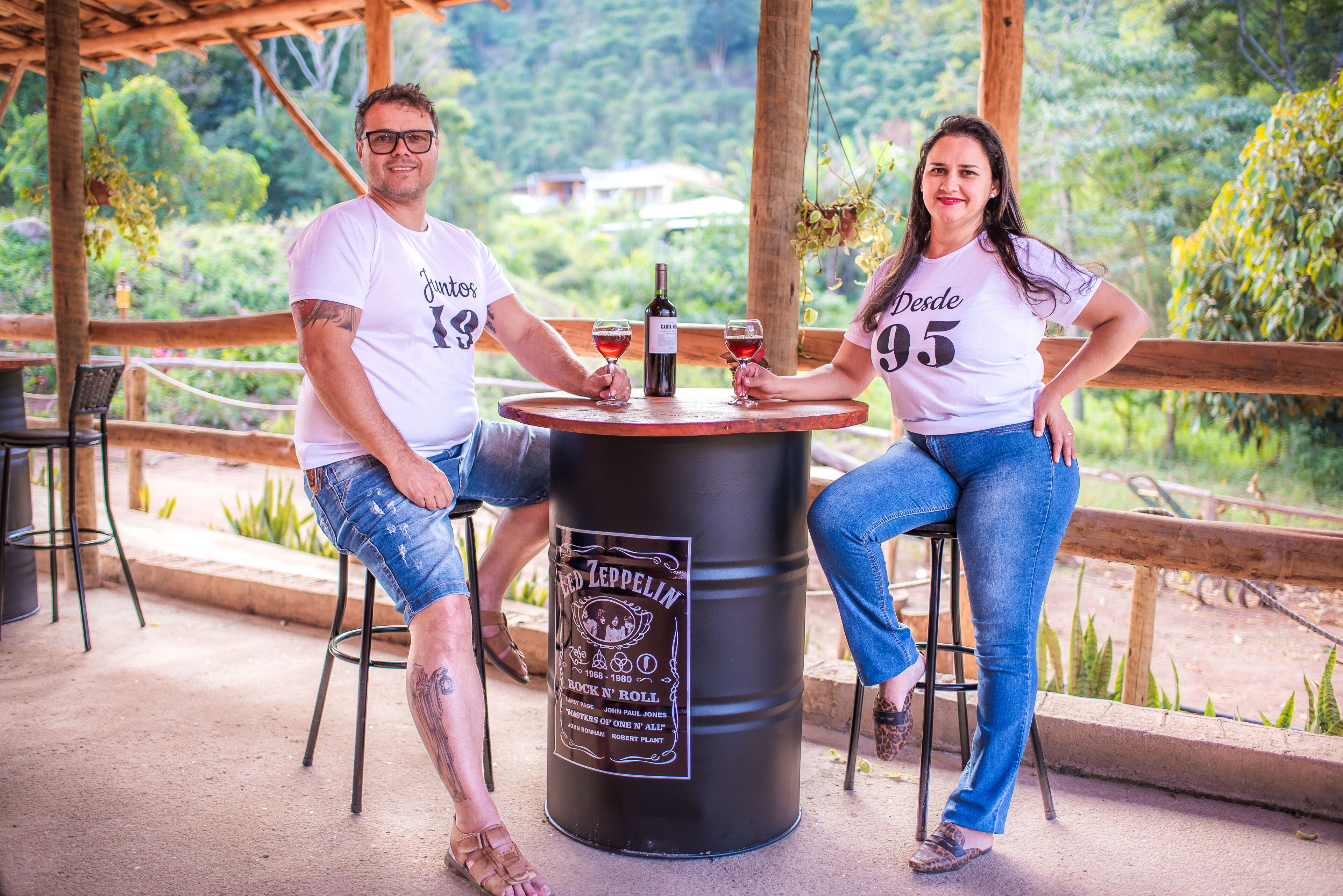 A couple seated at a round table with a beer barrel labeled 'Led Zeppelin' in a covered outdoor area with greenery in the background.