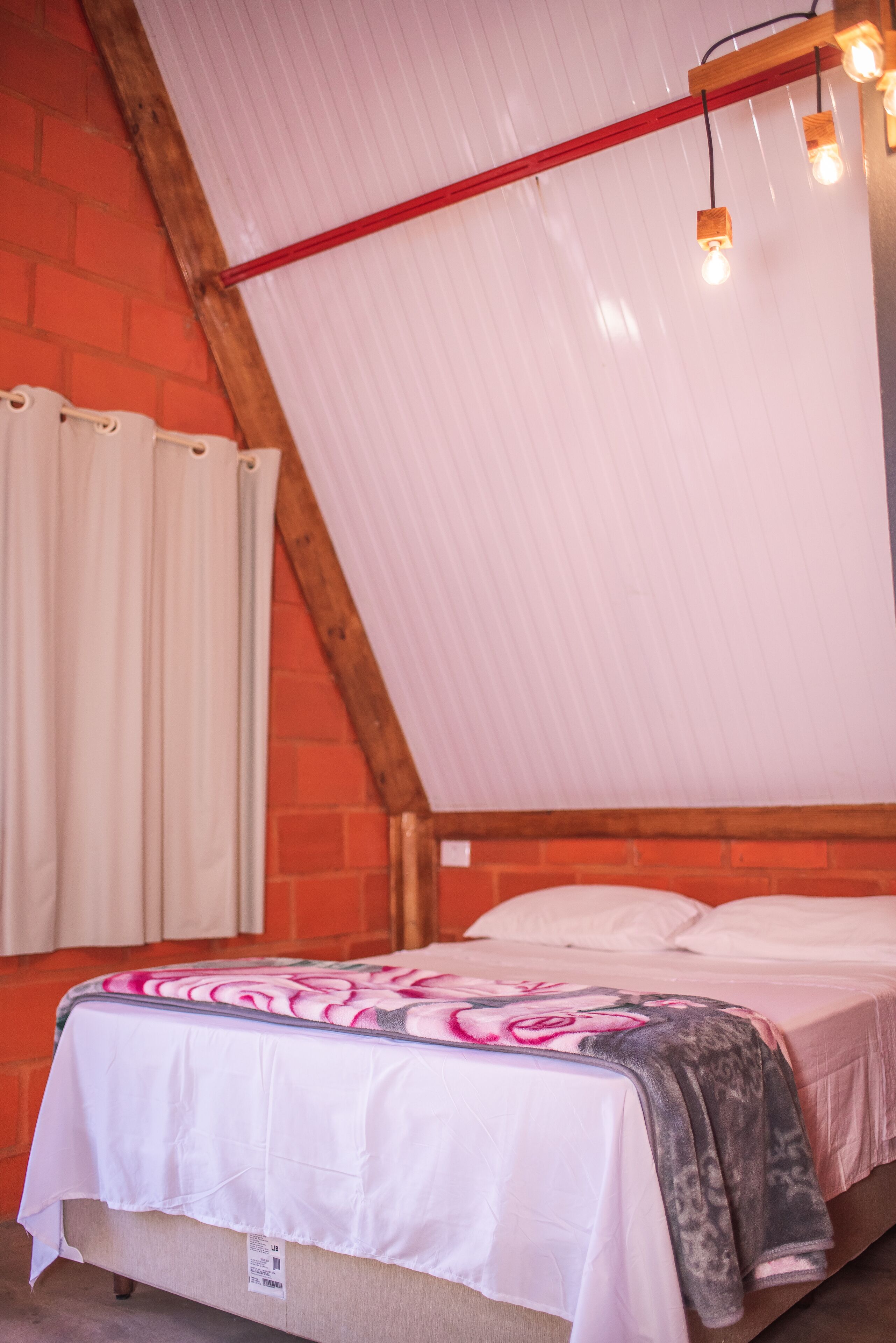 A bedroom with a wooden ceiling, a bed with a floral bedspread, and a red beam.