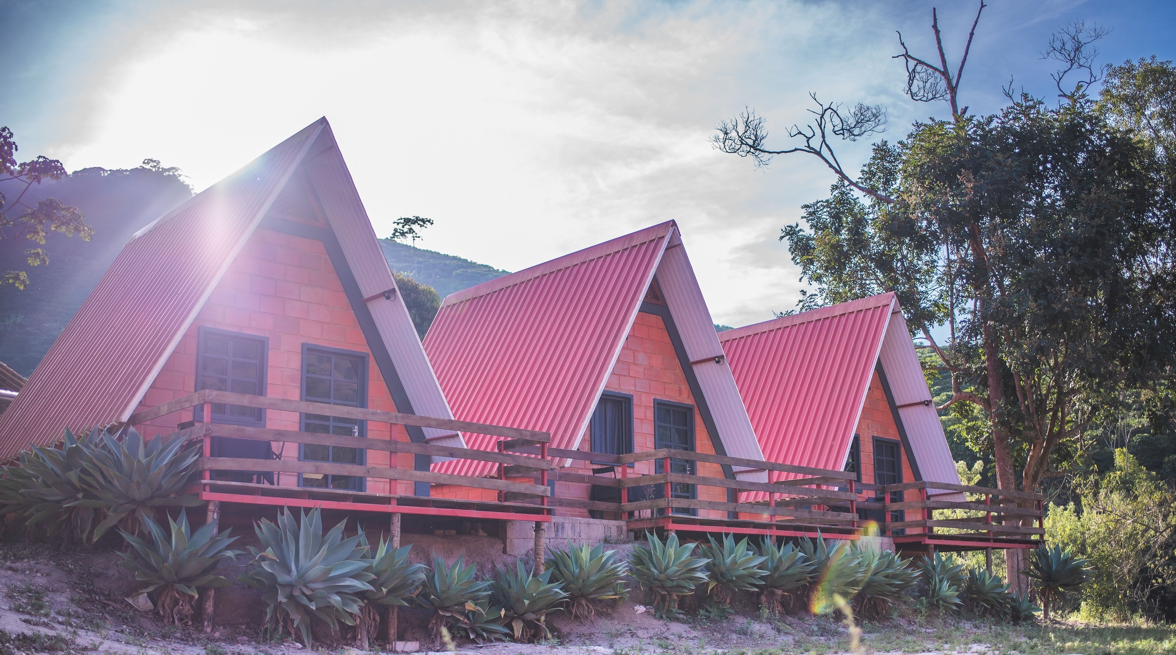 A modern building with a unique triangular roof design, surrounded by lush greenery and a mountainous backdrop.