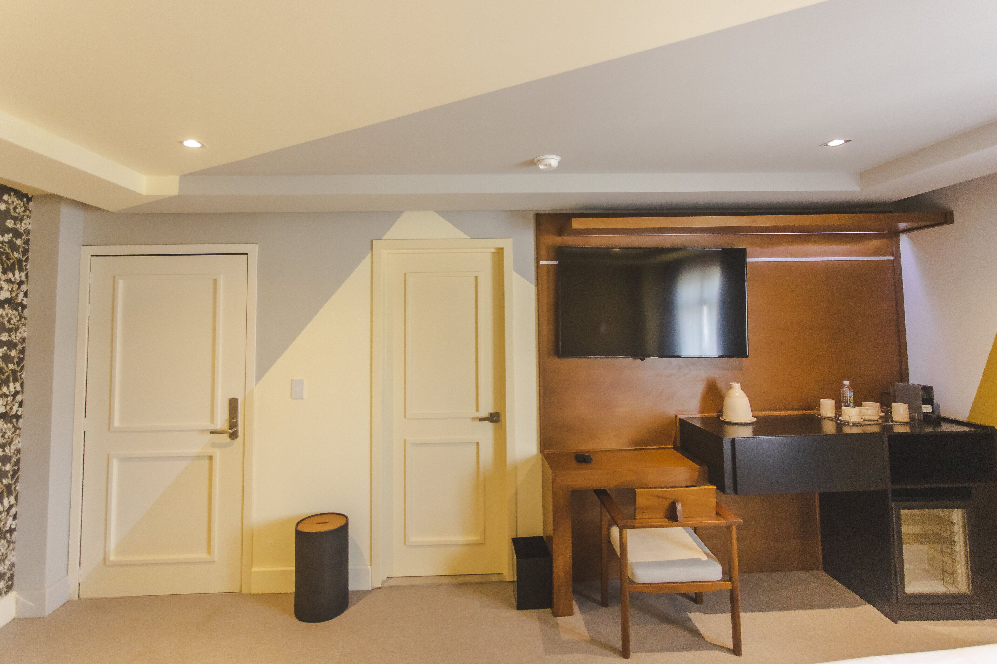 Ein Hotelzimmer mit einem Holztisch, einem an der Wand montierten Fernseher und einer Tür mit weißem Rahmen.