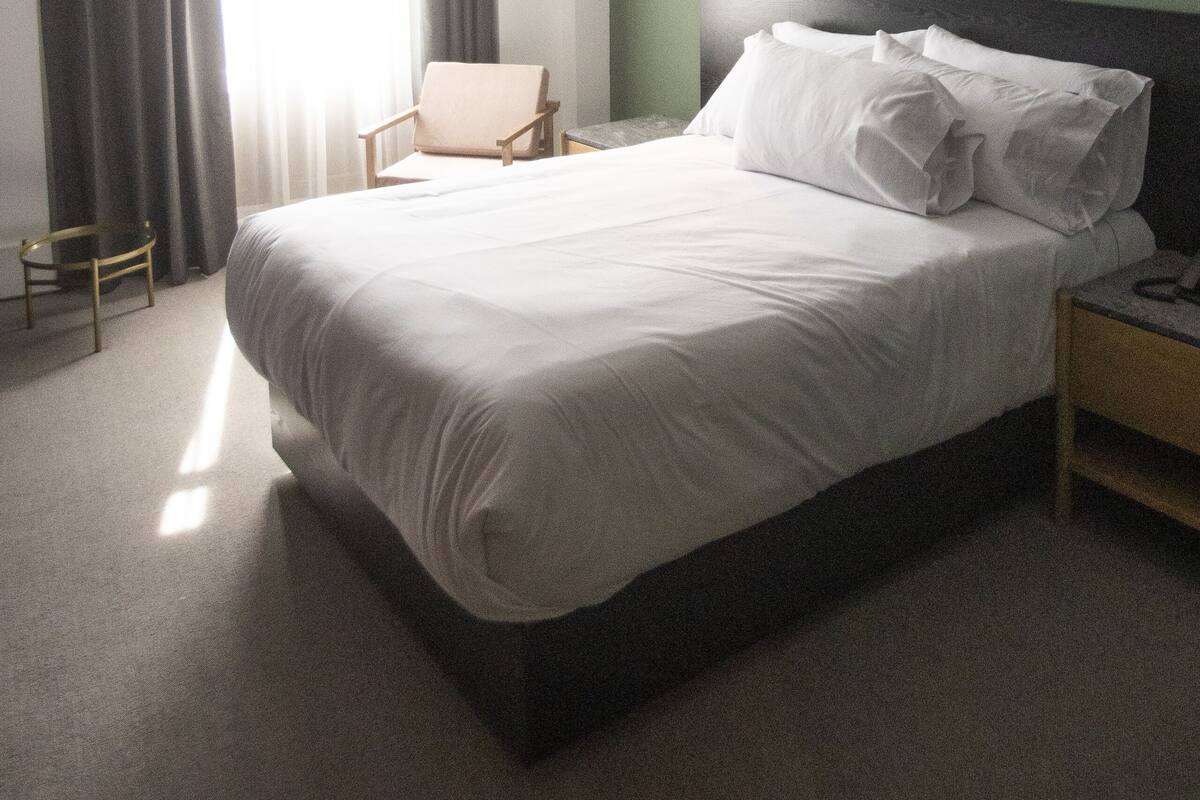 A hotel room with a large bed, a chair, a nightstand, and a window with curtains.
