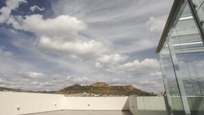 Une terrasse sur le toit offrant une vue dégagée sur une colline lointaine et un bâtiment moderne aux murs de verre.