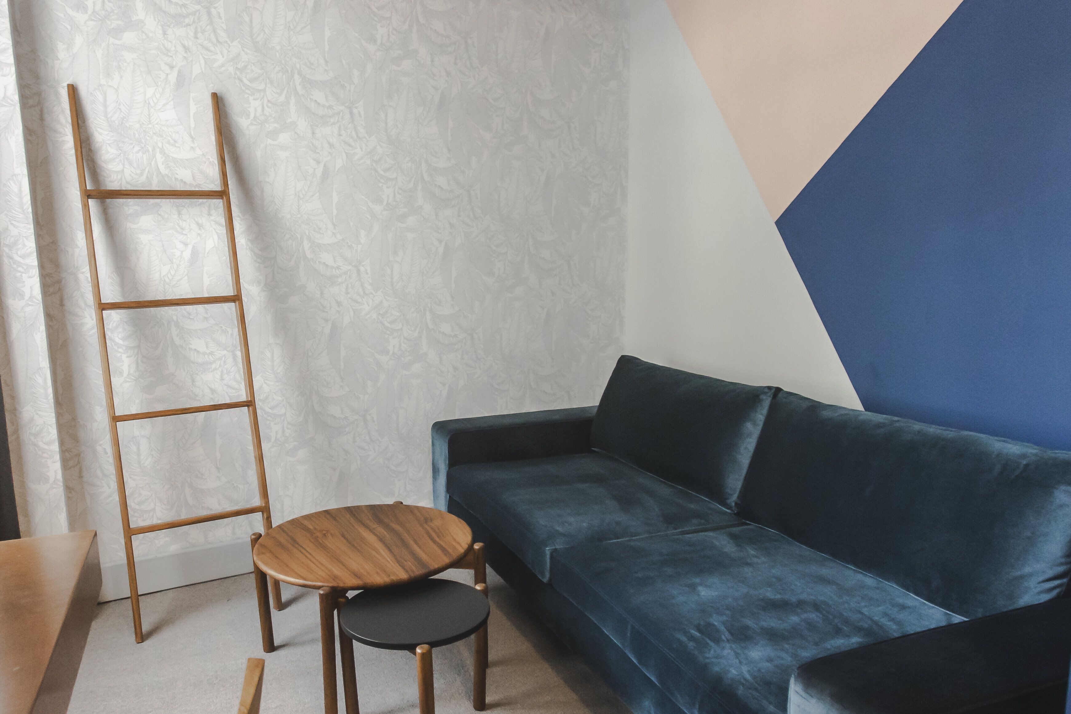 A room with a dark blue sofa, a wooden ladder, and a small round table with a black chair.
