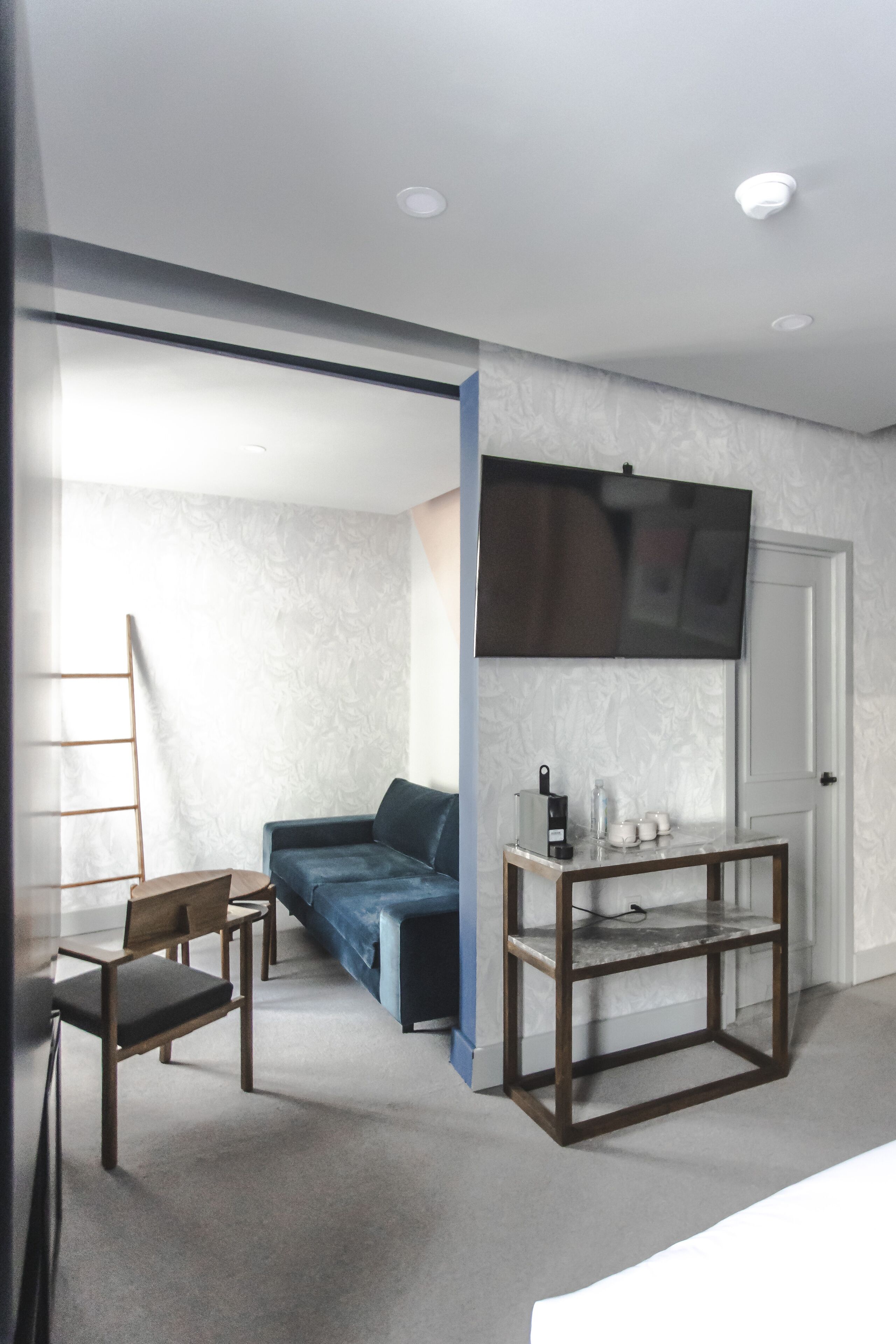 A room with a sofa, a coffee table, a TV mounted on the wall, and a door.