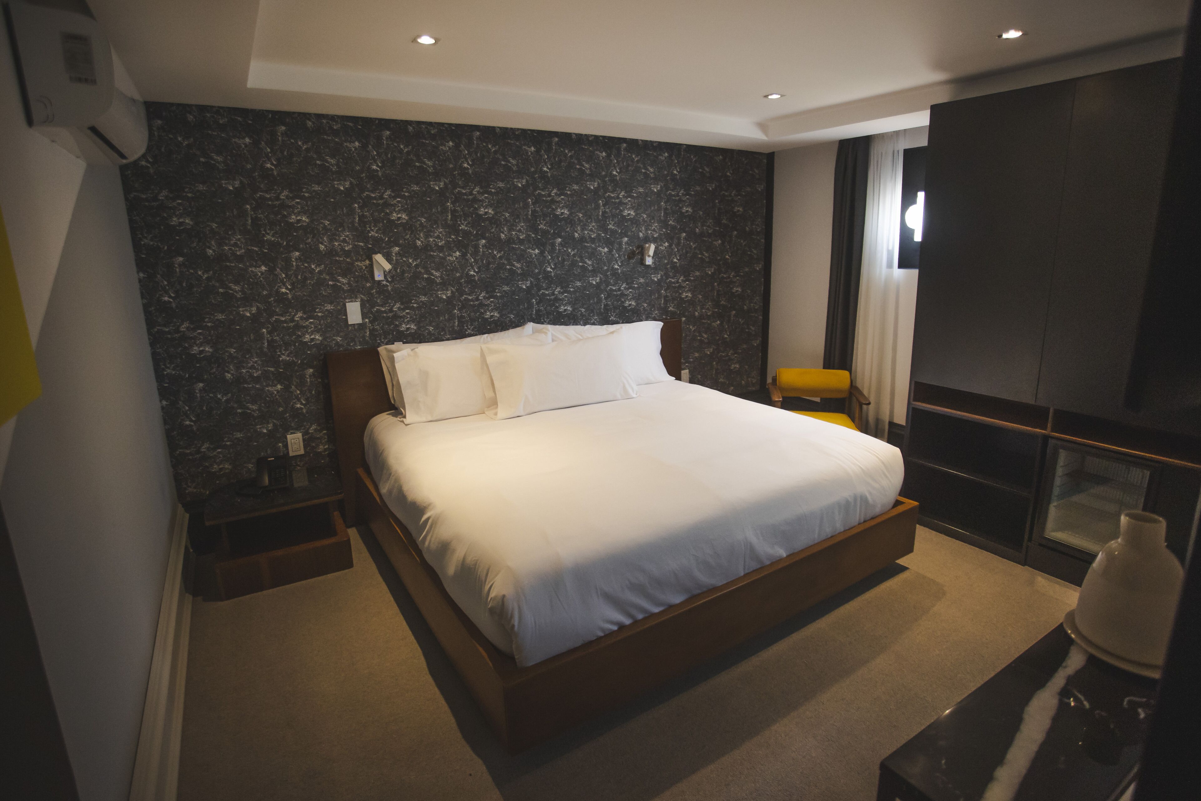 Una habitación de hotel moderna con una cama grande, un revestimiento de pared con diseño de mármol, una mesita de noche pequeña y un televisor integrado.