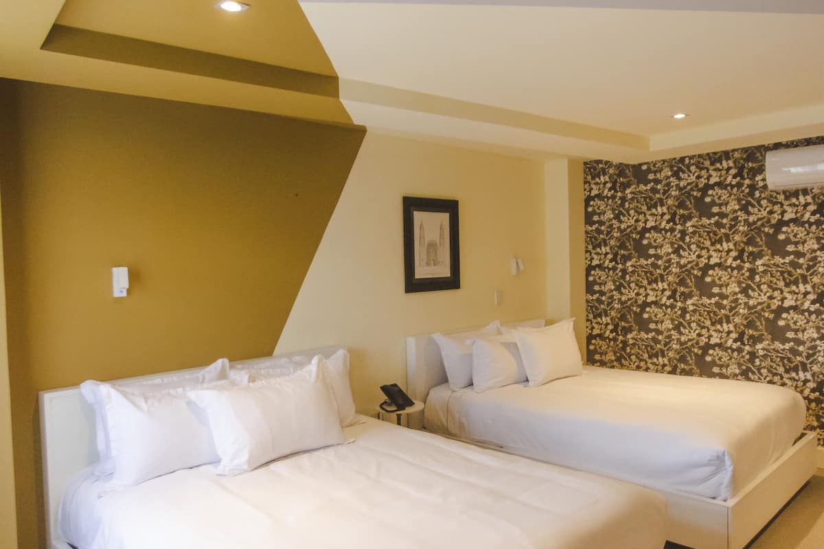 A hotel room with two beds, a wall-mounted air conditioner, and a framed picture on the wall.