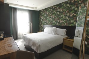 Hotelkamer met een groot bed, een bureau, een stoel, een nachtkastje met een telefoon en een spiegel.