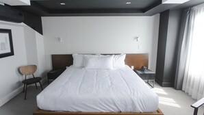 Une chambre d’hôtel moderne avec un grand lit, une tête de lit en bois, une table de chevet avec un téléphone et une chaise.
