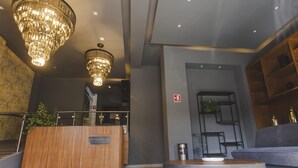 Un espace d’accueil moderne avec un comptoir de réception en bois, deux grands lustres, un canapé gris et une petite table sur laquelle se trouve un objet blanc.