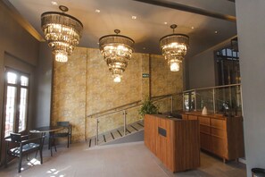 Un vestíbulo con una recepción, una escalera y tres candelabros.