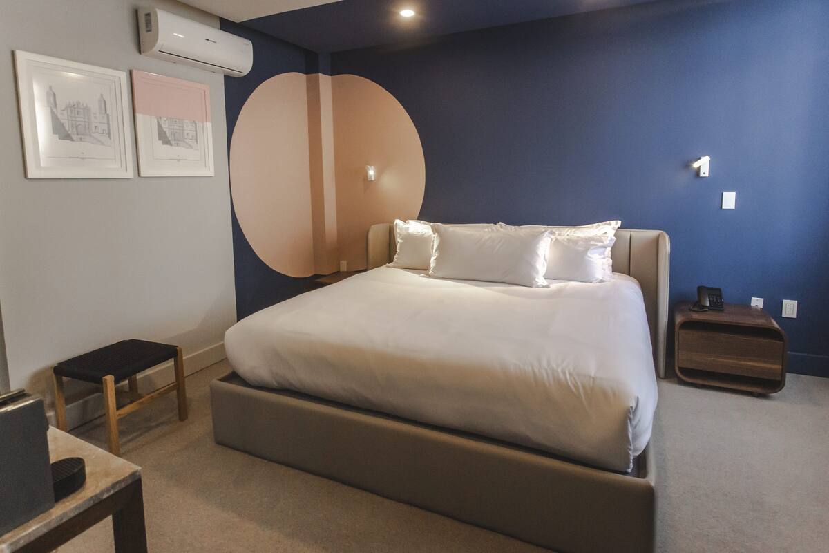 A bedroom with a bed, bedside tables, a wall-mounted air conditioner, and framed pictures.
